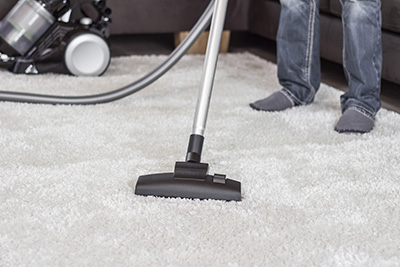 A man cleans the carpet with a vacuum cleaner.